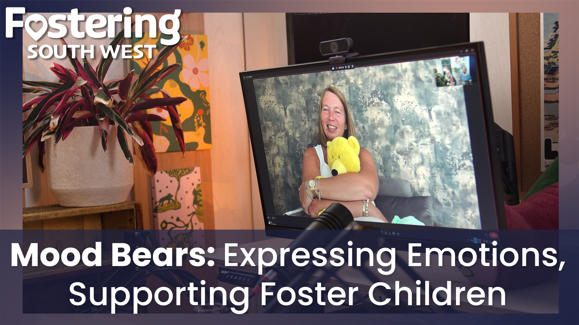 The image is a promotional graphic for Fostering South West, highlighting a podcast or video discussion about Mood Bears. It shows a computer monitor on a desk with a video call in progress. On the screen, a person is holding a bright yellow Mood Bear, which is a plush toy designed to help children express emotions and build resilience. In the foreground, there is a microphone positioned for recording, suggesting a podcast or interview setup. To the left, a decorative plant adds a touch of color to the scene.
Text on the image reads:
“Mood Bears: Expressing Emotions, Supporting Foster Children”
The overall design conveys a warm, supportive atmosphere and emphasizes the role of Mood Bears in promoting emotional wellbeing for foster children.
